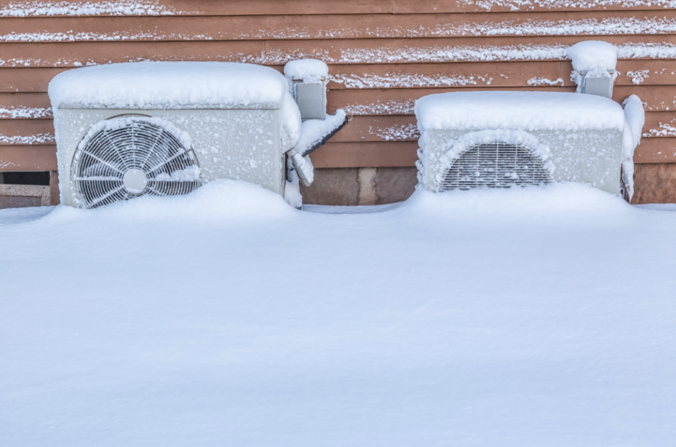 two heat pumps outside house covered in snow