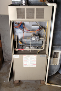 Exposed interior components of a beige gas furnace in a home basement.
