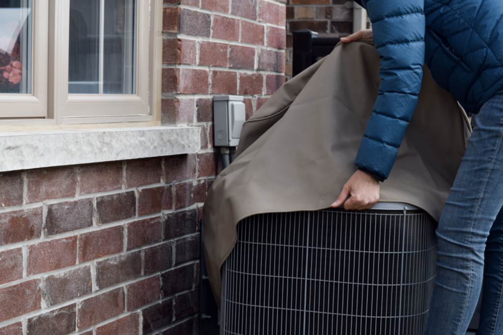 person putting cover on air conditioner unit outside of house