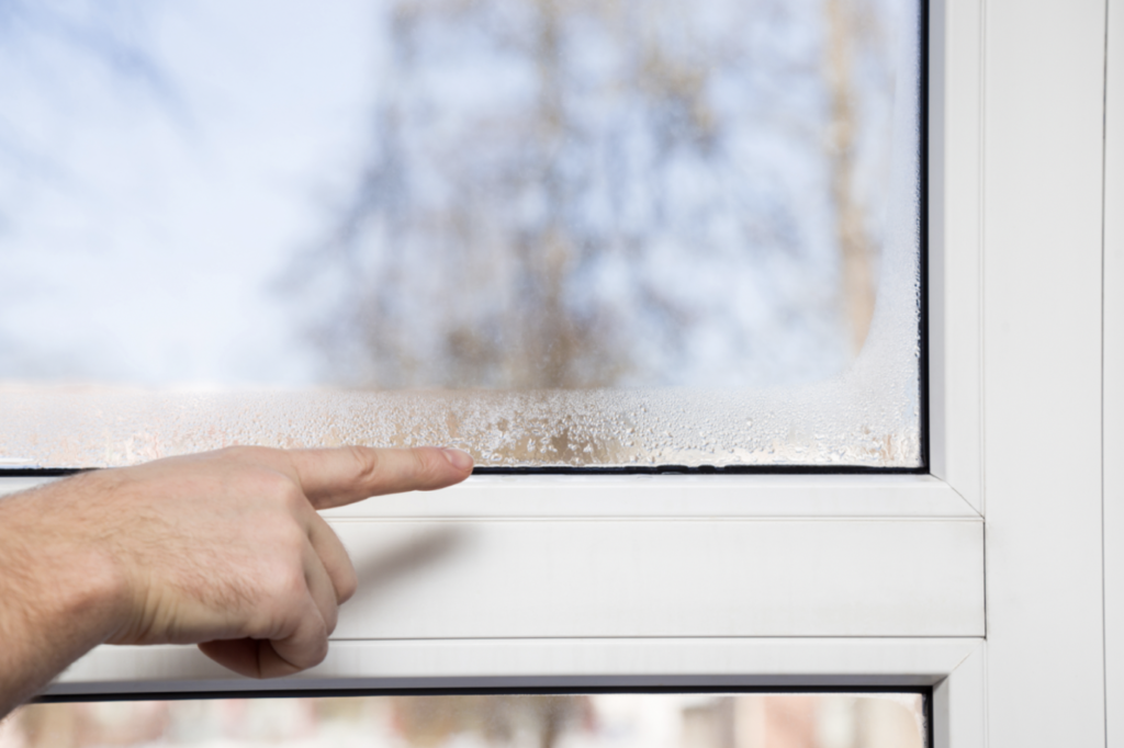 person points to condensation on inside of window of home
