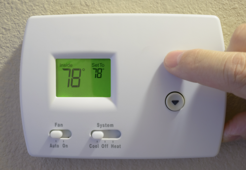 person's hand increases temperature on thermostat on wall to read 78 degrees fahrenheit.